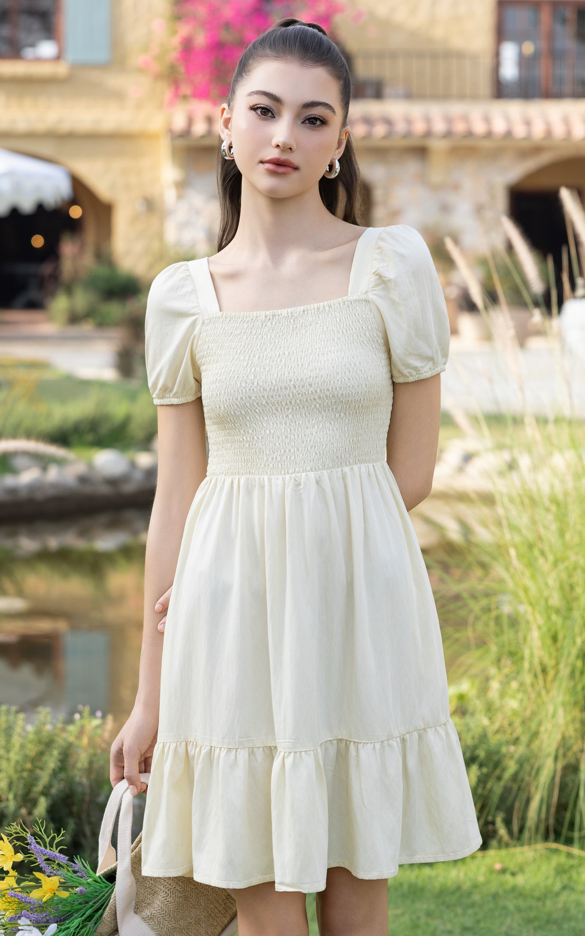 Woman in a white dress standing outdoors with greenery and a building in the background